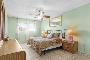A bedroom with a bed, bedside lamps, a nightstand, a dresser, a ceiling fan, and a window with curtains. - Serene 2-bedroom condo with AC in beautiful Cape Coral (Cape Coral)