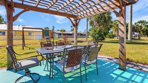 Ein überdachter Außenbereich mit Tisch und Stühlen, umgeben von einer Holzpergola.