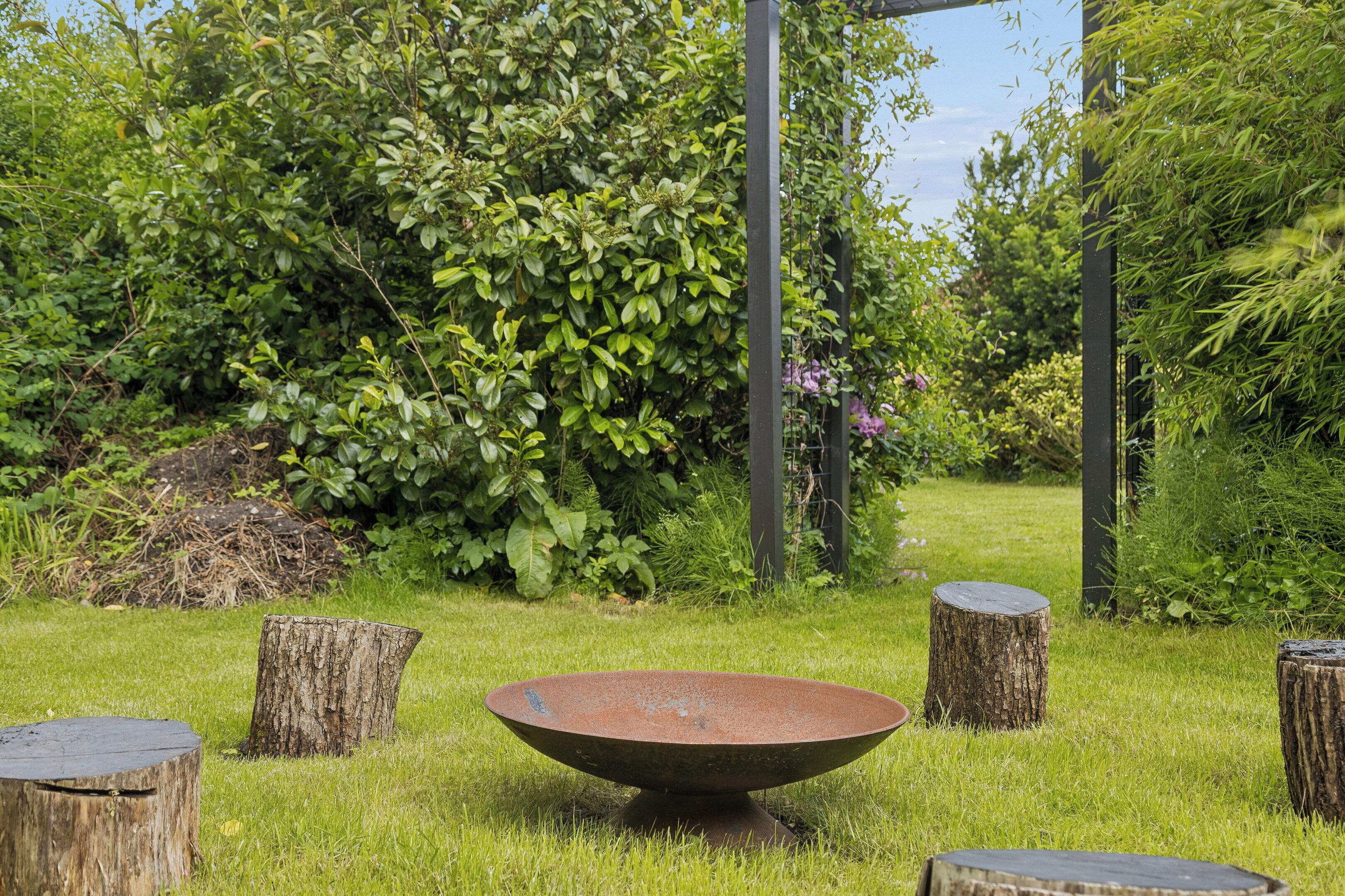 A garden with a central metal bowl, surrounded by wooden stumps and lush greenery.