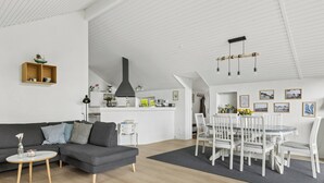 Ein modernes Wohnzimmer mit einem grauen Sofa, einem kleinen runden Tisch und einem Essbereich mit weißen Stühlen und einem Glastisch.