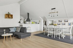 A modern living room with a grey sofa, a small round table, and a dining area with white chairs and a glass table. - Lovely holiday home 350 meters from Høll Strand (Børkop)