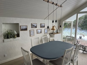 A dining area with a round table, white chairs, a hanging light fixture, and framed pictures on the wall. - Lovely holiday home 350 meters from Høll Strand (Børkop)