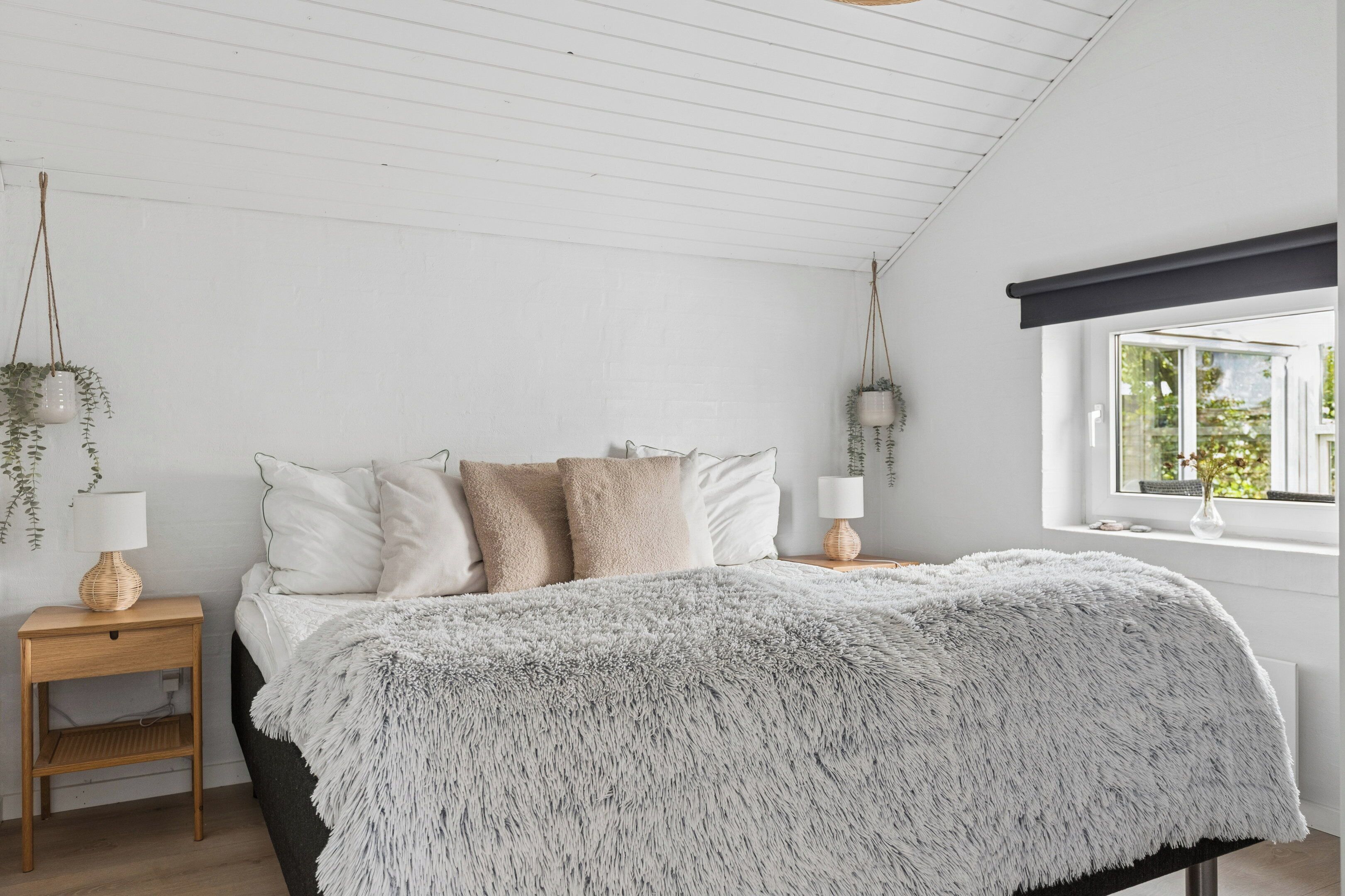 Ein Schlafzimmer mit Bett, Nachttischen, hängenden Pflanzen und einem Fenster.