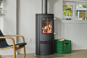 A modern interior with a black wood-burning stove, a green crate with logs, and a chair. - Lovely holiday home 350 meters from Høll Strand (Børkop)