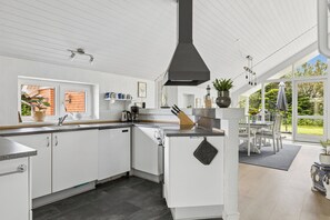 A modern kitchen with white cabinets, a black range hood, and a dining area with a table and chairs. - Lovely holiday home 350 meters from Høll Strand (Børkop)