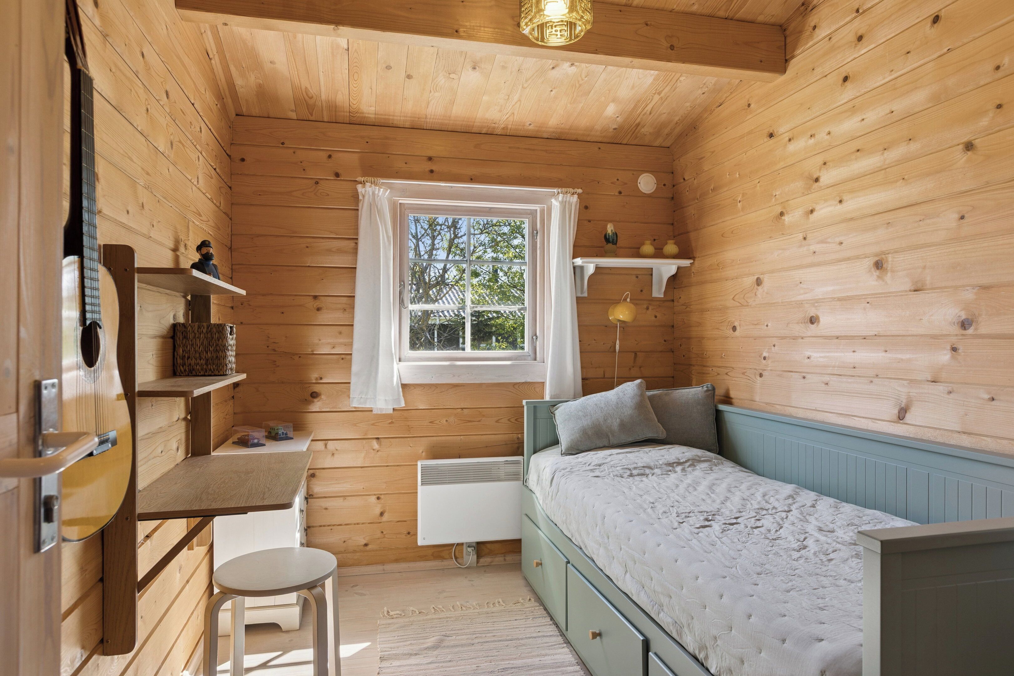 Une pièce de style cabane en bois, comprenant un lit, un bureau, une chaise, une fenêtre et une étagère avec des objets décoratifs.