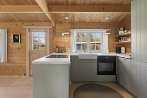 Una cocina con paredes de madera, un lavamanos, una estufa y una ventana con cortinas.