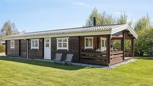 Een houten blokhut met een overdekte veranda, twee ramen en een schoorsteen.