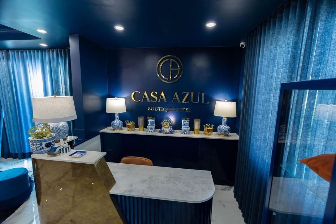 Et hotelreception område med et blåt farvetema, en receptionsdisk og et skilt på væggen, der lyder 'CASA AZUL BOUTIQUE HOTEL'.