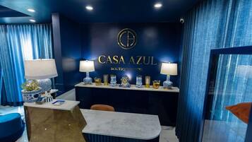 Et hotelreception område med et blåt farvetema, en receptionsdisk og et skilt på væggen, der lyder 'CASA AZUL BOUTIQUE HOTEL'.