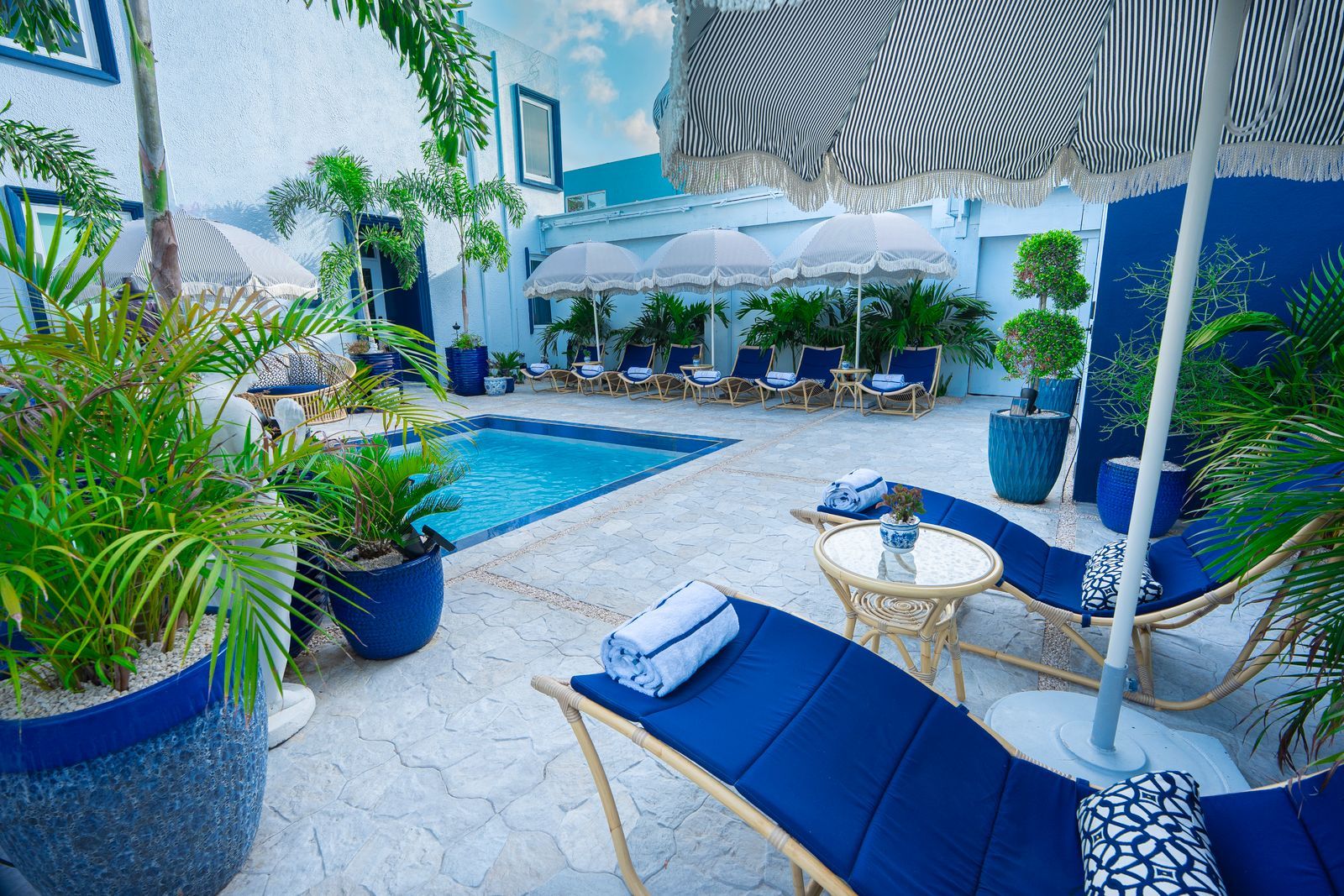 Zona de piscina con sillones de descanso, sombrillas y plantas en macetas.
