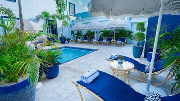 Zona de piscina con sillones de descanso, sombrillas y plantas en macetas.