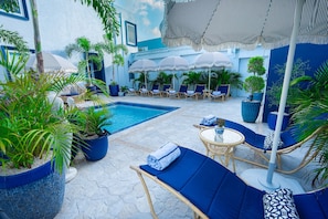 A poolside area with lounge chairs, umbrellas, and potted plants.