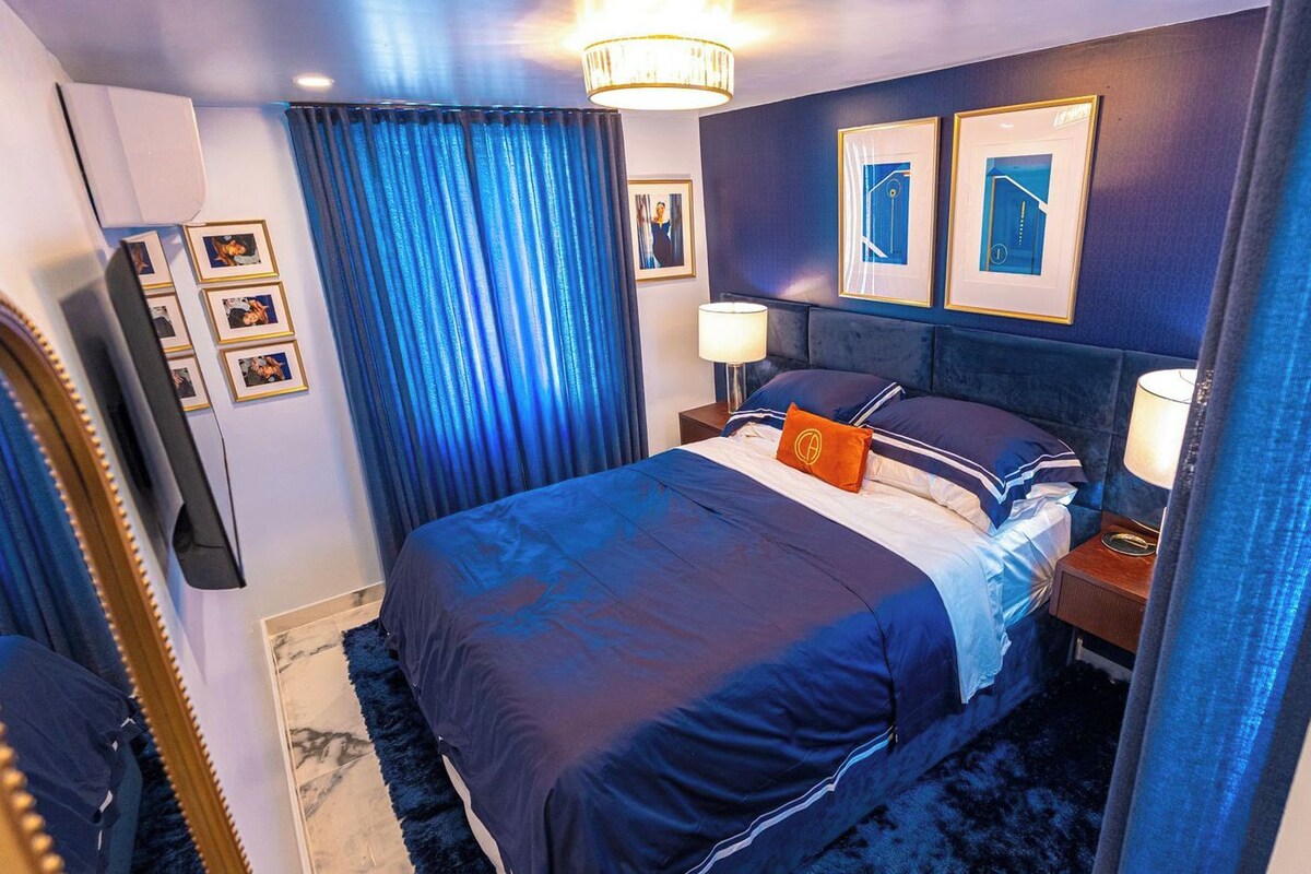 A hotel room with a bed, a nightstand, a lamp, a mirror, and framed pictures on the wall.