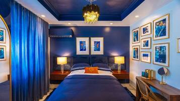 Habitación de hotel con una cama grande, dos mesitas de noche con lámparas, un escritorio con silla y cuadros en la pared.