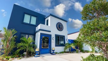 Un edificio moderno de dos pisos con una combinación de colores azul y blanco, un logotipo destacado en la fachada y un jardín bien cuidado con palmeras.