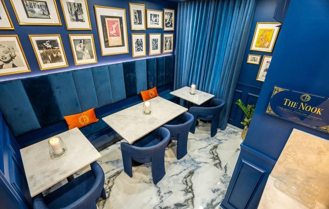 Una habitación con asientos tapizados en azul, cuadros en la pared y un letrero que dice 'The Nook'.