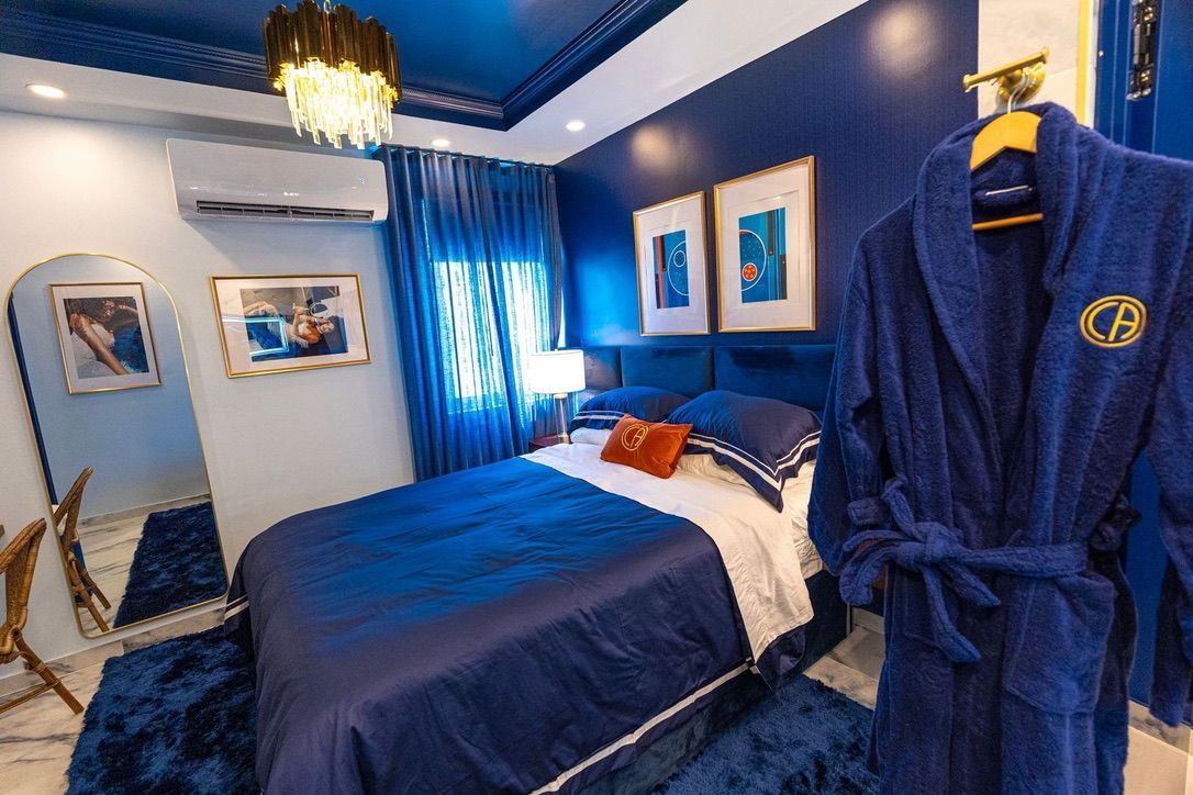 A bedroom with a large bed, a robe hanging on a rack, and a chandelier.