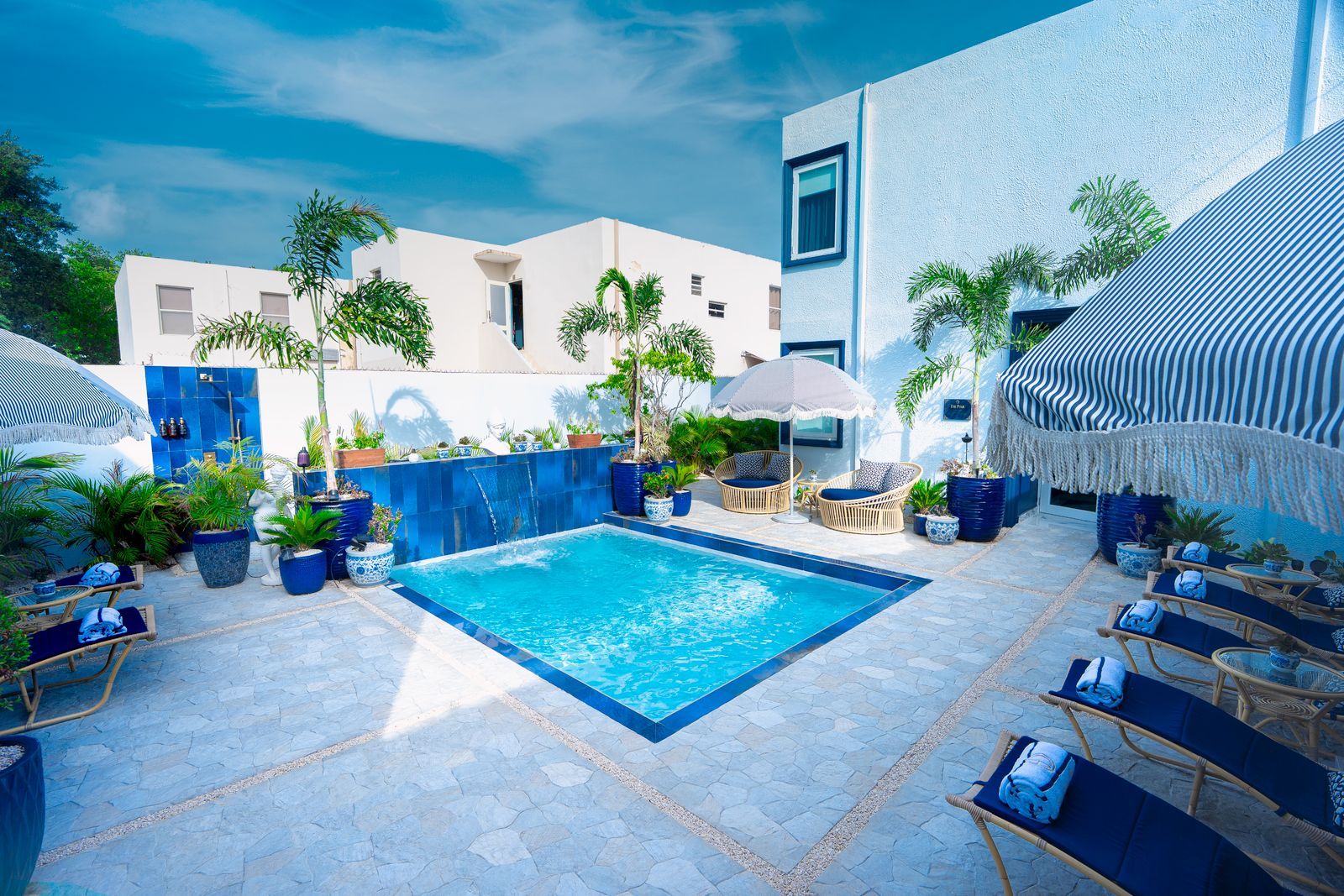 Un área de piscina con sillas de descanso, plantas en macetas y un cielo azul despejado.