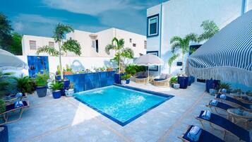 Un área de piscina con sillas de descanso, plantas en macetas y un cielo azul despejado.