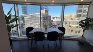 A modern dining area with a wooden table and black chairs, large windows offering a city view, and a potted plant on the right. - Waterfront, large 2 BR & 2 Bath with 6 appliances (Halifax)