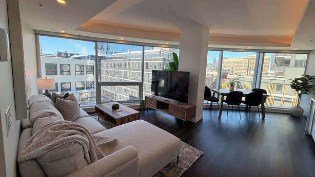 A modern living room with a large sofa, a TV, and a dining area with chairs and a table. - Waterfront, large 2 BR & 2 Bath with 6 appliances (Halifax)