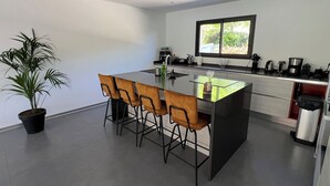 A modern kitchen with a central island, four bar stools, a potted plant, and a window with a view of greenery. - NEW VILLA WITH POOL, WIFI, NEAR ILE ROUSSE (VILLE DI PARASO)