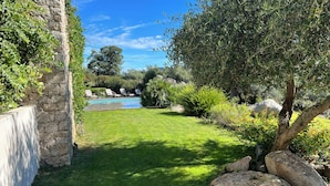 A stone wall with a pool, green grass, and various plants. - NEW VILLA WITH POOL, WIFI, NEAR ILE ROUSSE (VILLE DI PARASO)