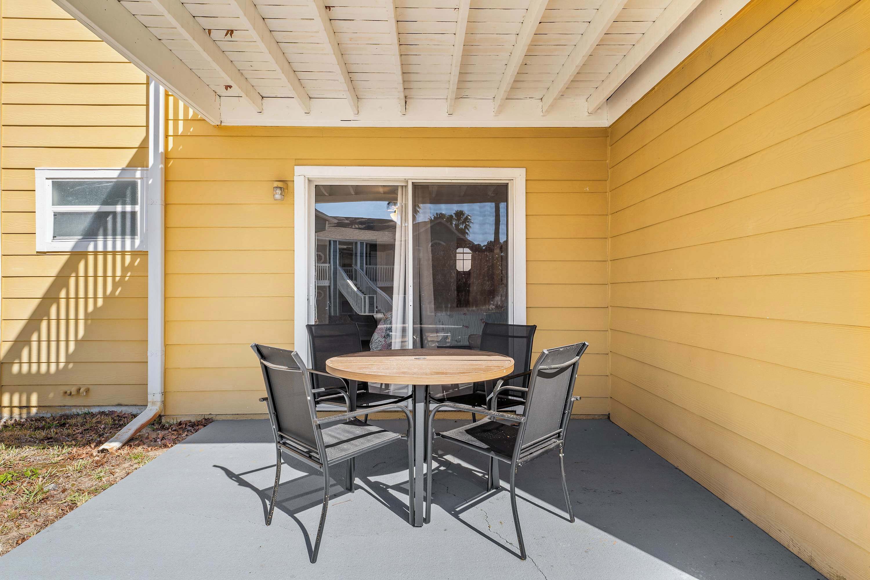 Une terrasse avec une table ronde et quatre chaises, une porte-fenêtre coulissante et une façade jaune.