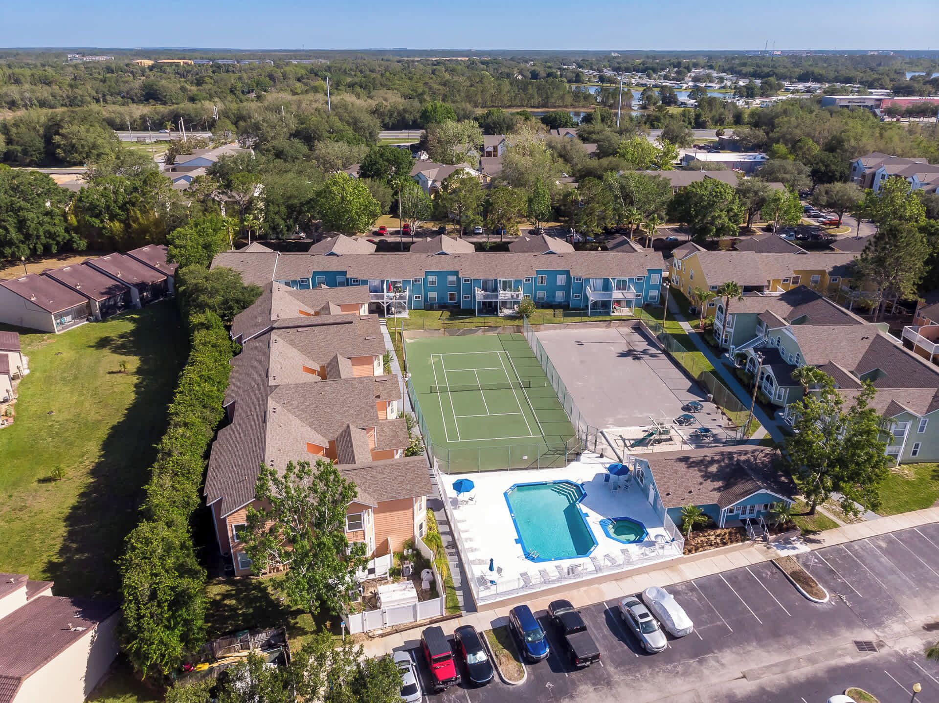 An aerial view of a residential area with houses, a tennis court, and a swimming pool.