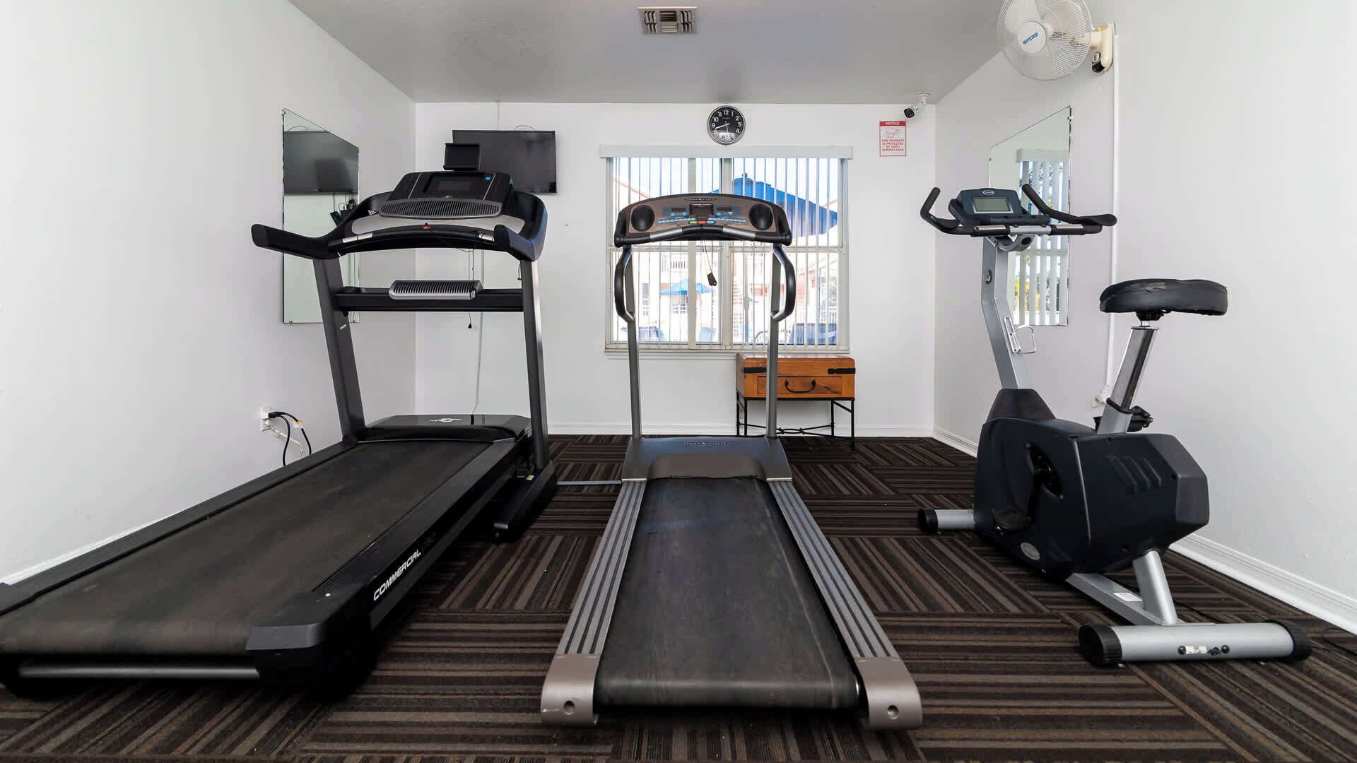 Une salle de sport équipée de tapis de course, d’un appareil d’escalier et d’un vélo elliptique.