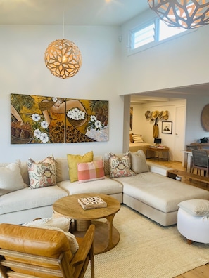 A modern living room with a sectional sofa, a wooden coffee table, and a large abstract painting. - Classic Aussie beach house with amazing views and pet friendly garden. (Ulladulla)