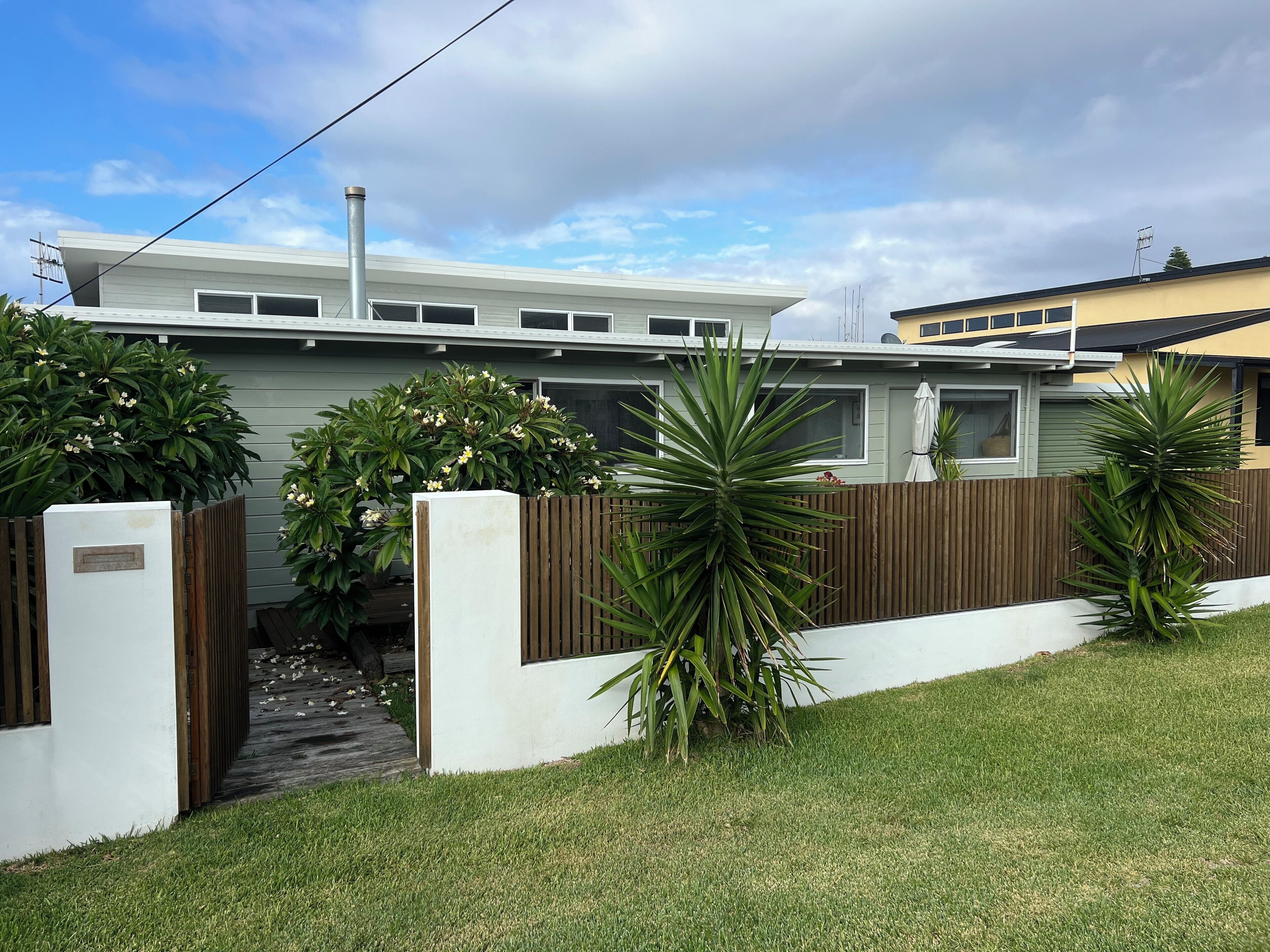 A modern house with a fenced yard, a wooden gate, and a pathway leading to the entrance.