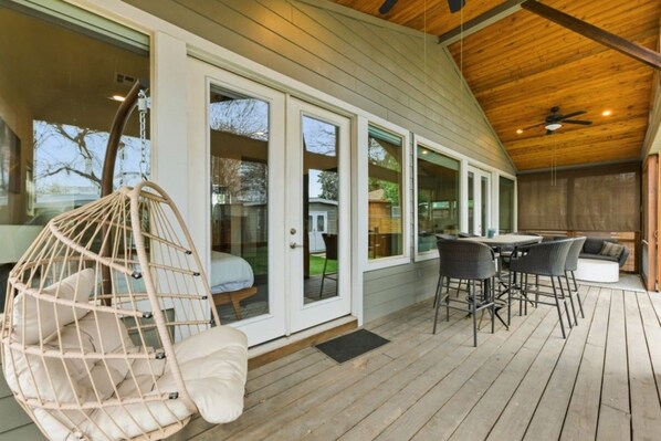 A covered outdoor area with a wooden deck, a hanging chair, and a table with chairs.