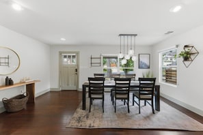 A dining area with a table and chairs, a hanging light fixture, and a window with blinds.