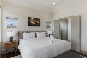 A hotel room with a large bed, two bedside tables with lamps, a painting on the wall, and a door to the right.