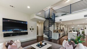 Een ruime woonkamer met een grote flatscreen-tv, een moderne trap en een keukenhoek.