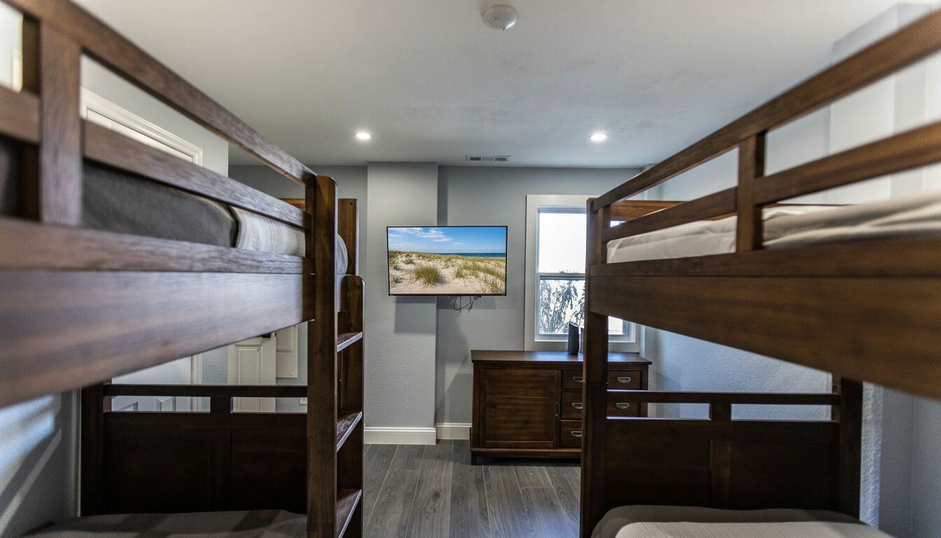 A bunk bed room with a television on the wall, a window with a view, and a wooden dresser.