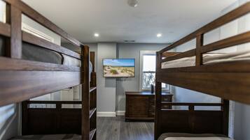 A bunk bed room with a television on the wall, a window with a view, and a wooden dresser.