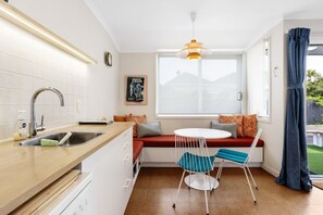 A compact kitchen with a sink, a window seat with a table and chairs, and a pendant light. - Retro Retreat | Walk to St Clair Beach (Dunedin)
