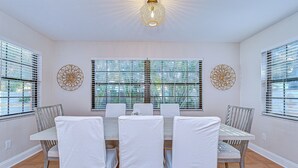 A dining area with a table set for six, white chairs, and decorative wall art. - Terracotta Tides • 175 Steps to Indian Rocks Beach • Sleeps 6 • Sunrise & Sunset (Indian Rocks Beach)