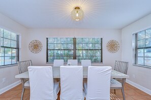 A dining area with a table set for six, white chairs, and decorative wall art. - Terracotta Tides • 175 Steps to Indian Rocks Beach • Sleeps 6 • Sunrise & Sunset (Indian Rocks Beach)