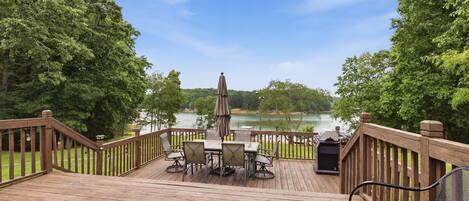 A wooden deck with a table and chairs, overlooking a lake.