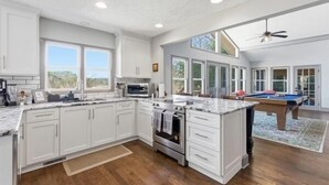 Una cocina amplia con gabinetes blancos, una isla grande y una mesa de billar.