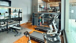 Un gimnasio con cintas de correr, máquinas de pesas y techo de madera.