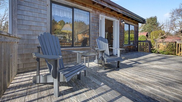 A wooden deck with Adirondack chairs and a table, overlooking a residential area. - Coastal Escape with Fireplace, Three Decks & Easy Beach Access (Cannon Beach)