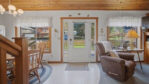 A cozy living room with a wooden ceiling, a brown leather armchair, a wooden coffee table, and a view of a backyard through a glass door. - Coastal Escape with Fireplace, Three Decks & Easy Beach Access (Cannon Beach)