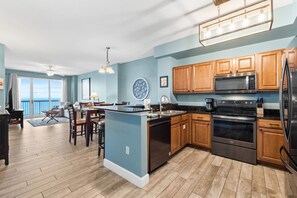 A modern kitchen with wooden cabinets, stainless steel appliances, and a dining area with a view. - Fall Deals + Snowbird Rates | Gulf Front Beach Escape (Panama City Beach)