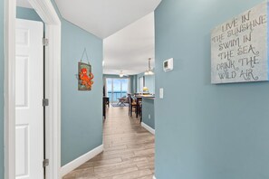 A hallway with light blue walls, wooden flooring, and a dining area with a table and chairs. - Fall Deals + Snowbird Rates | Gulf Front Beach Escape (Panama City Beach)
