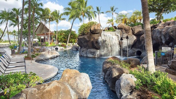 Ein Resort-Pool mit Wasserfall, umgeben von Felsen und Palmen.